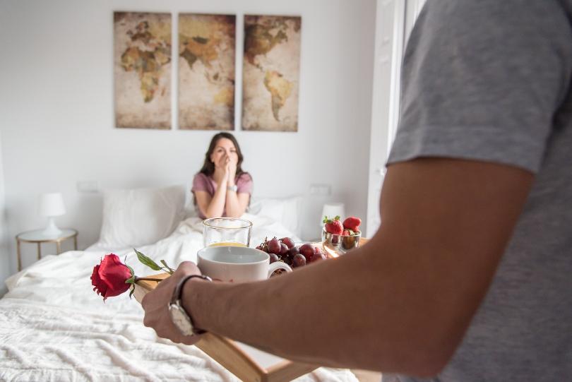 Mann bringt romantisches Frühstück ans Bett - Hochzeitstag feiern in Zeiten von Einschränkungen