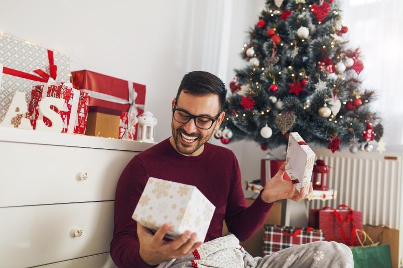 Junger Mann öffnet fröhlich ein Weihnachtsgeschenk - Geschenke zu Weihnachten