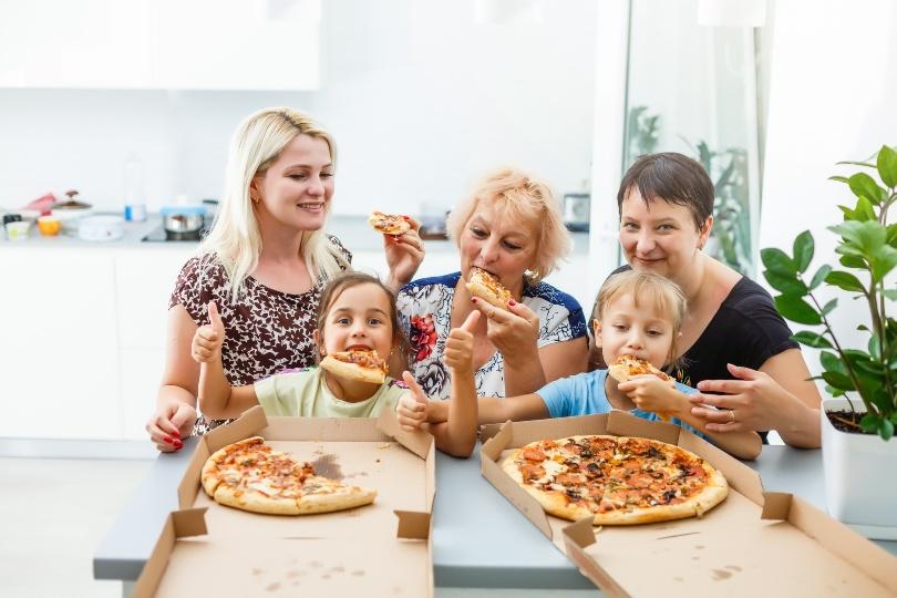 Zwei Kinder, die Mutter und 2 Großmütter essen Pizza - vielleicht ist es eine Einschulungsparty