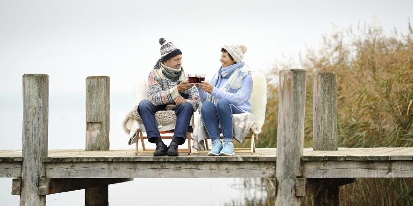 Älteres Paar sitzt auf einem Steg und trinkt Glühwein - Glühweinparty 
