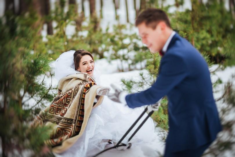 Hochzeitspaar, Mann zieht Frau auf Schlitten durch den Schnee