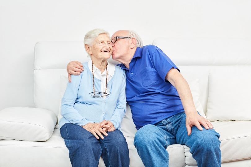 Altes Paar auf Sofa - Mann gibt Frau einen Kuss